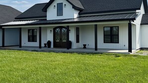 Uma casa de dois andares com fachada simétrica, uma entrada central com porta escura e varanda coberta com plantas em vasos.