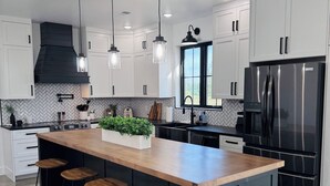 Cozinha moderna com ilha central, banquetas, geladeira preta e iluminação pendente.