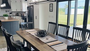 Cozinha moderna com armários brancos, mesa de jantar de madeira, cadeiras pretas e uma janela grande com vista para o exterior.