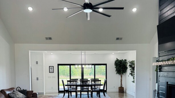 Uma sala de estar espaçosa com ventoinha no teto, área de jantar com mesa e cadeiras, e lareira.