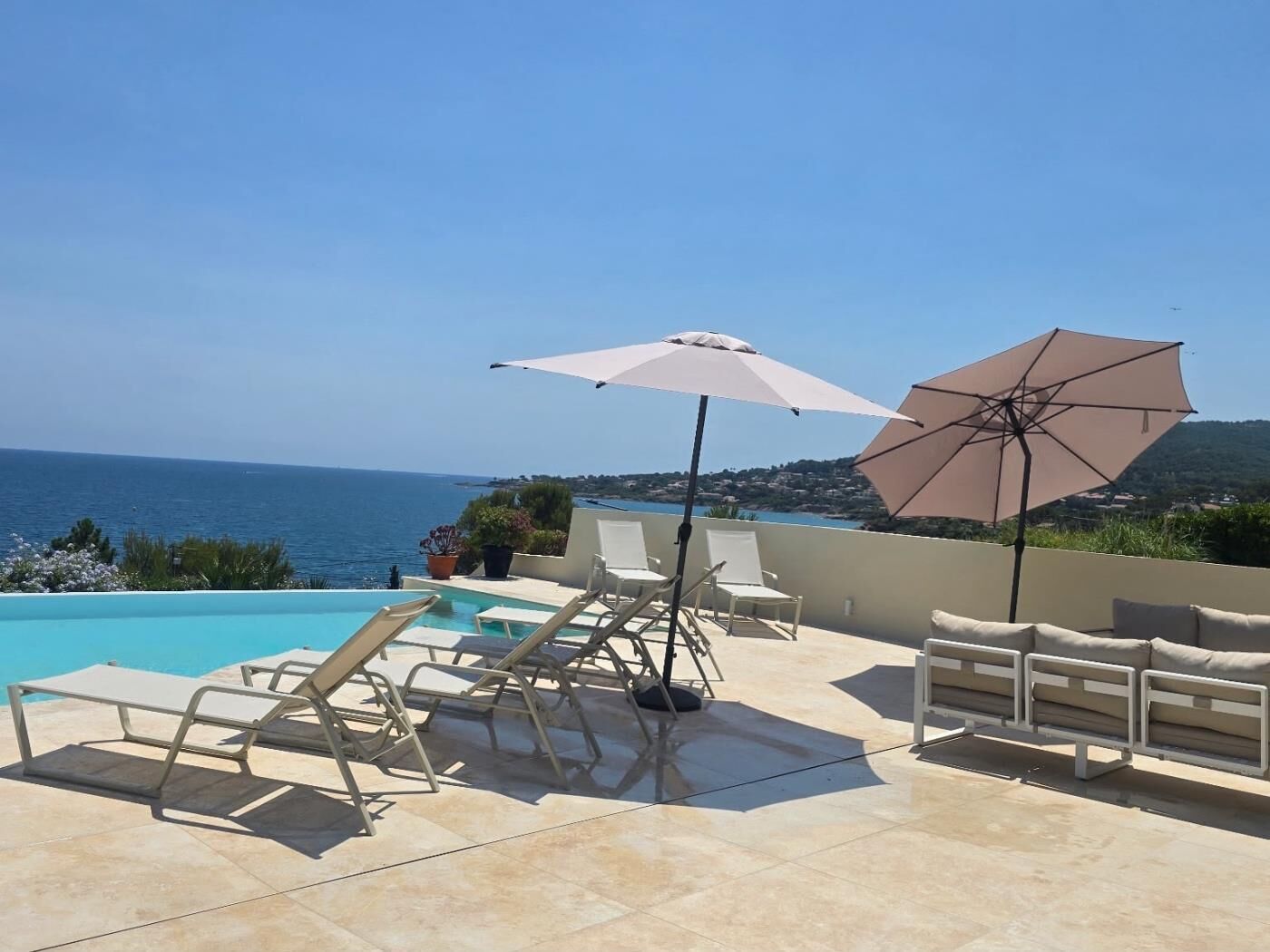 Zona de piscina con sillones de descanso y sombrillas, con vista a una masa de agua y un paisaje montañoso.