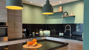 A modern kitchen with a central island, black countertops, wooden cabinets, and pendant lighting. - 5-bedroom house, sea view, swimming pool (Fréjus)