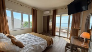 A hotel room with a bed, a desk, a chair, a TV, and a balcony with a view of the sea. - 5-bedroom house, sea view, swimming pool (Fréjus)