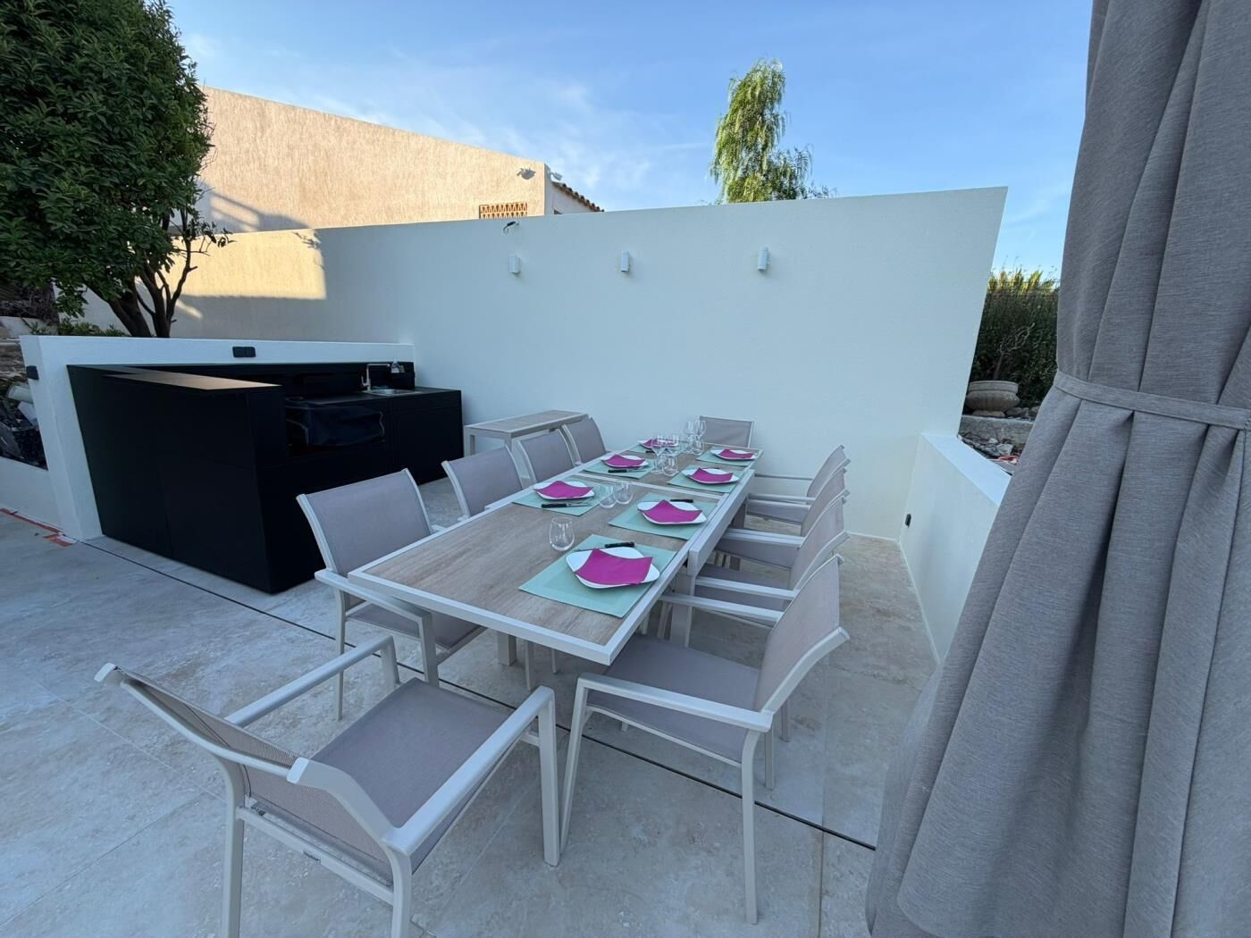 Une terrasse extérieure avec une table dressée pour le repas, un barbecue et un mur blanc.