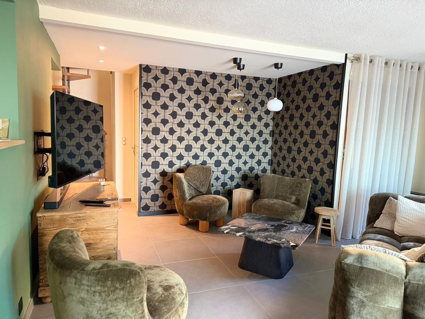 Een woonkamer met een televisie, twee fauteuils, een salontafel en behang met een patroon.