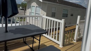 Een terras met een tafel en banken, een witte reling, en een huis op de achtergrond.