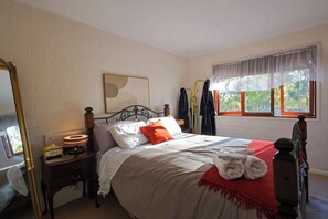 A bedroom with a bed, a nightstand, a mirror, a window with curtains, and a view of trees outside.