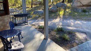 A covered patio with a table and chairs, surrounded by natural landscape and rocks. - Granite Garden Apartment - 2 Bedroom (Eukey)