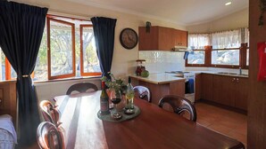 A dining area with a wooden table, chairs, a clock, and a kitchen in the background. - Granite Garden Apartment - 2 Bedroom (Eukey)