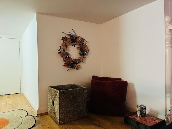 A corner room with a wooden floor, a woven storage box, a red cushion, and a decorative wreath on the wall. - 5 Minute Walk to St Paul s Cathedral (London)