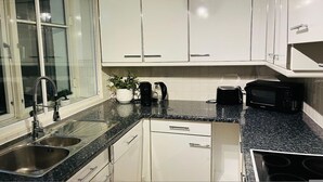 A modern kitchen with white cabinets, a granite countertop, stainless steel sink, and a black stove. - 5 Minute Walk to St Paul s Cathedral (London)