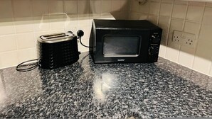 A kitchen with a black toaster and a black microwave on a granite countertop, white cabinets, and a tiled backsplash. - 5 Minute Walk to St Paul s Cathedral (London)