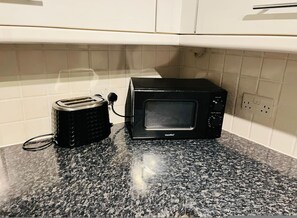 A kitchen with a black toaster and a black microwave on a granite countertop, white cabinets, and a tiled backsplash. - 5 Minute Walk to St Paul s Cathedral (London)