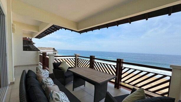 Ein Balkon mit Meerblick, ausgestattet mit einer Couch, Stühlen und einem Tisch.
