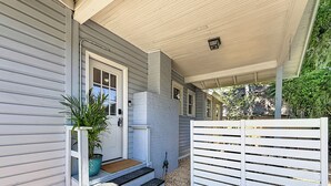 A covered porch with steps leading to a door, a potted plant, and a white fence. - The Peacock House - Vintage Downtown Charm (Ocala)
