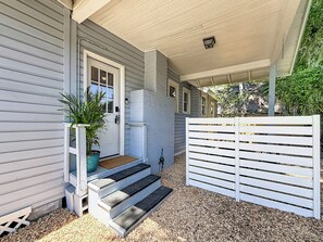 A covered porch with steps leading to a door, a potted plant, and a white fence. - The Peacock House - Vintage Downtown Charm (Ocala)