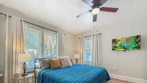 A bedroom with a bed, a ceiling fan, a TV on the wall, and a window with curtains. - The Peacock House - Vintage Downtown Charm (Ocala)