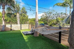 A hammock between trees in a backyard with artificial grass and wooden fencing.