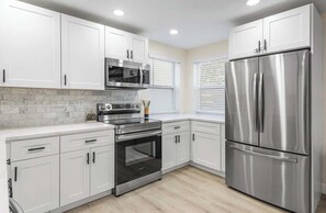 A modern kitchen with white cabinets, stainless steel appliances, and a marble backsplash.