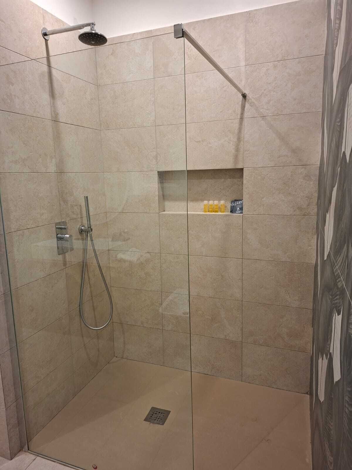 Une douche à l’italienne avec un pommeau de douche à main et une étagère pour les articles de toilette.
