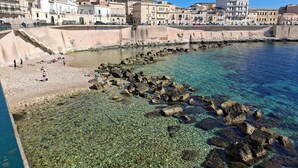 A coastal town with clear waters, rocky shoreline, and historic buildings. - Armonia sul mare (Syracuse)