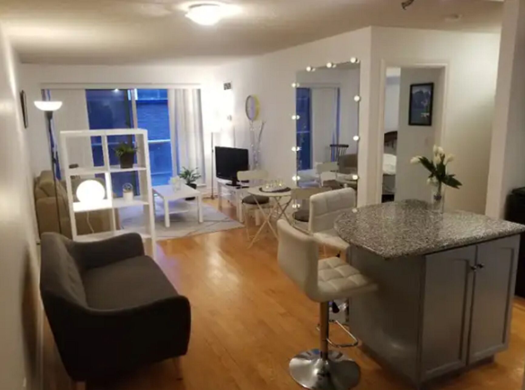Una sala moderna con un sofá, un comedor con mesa y sillas, una cocina con barra, y un balcón con vistas.