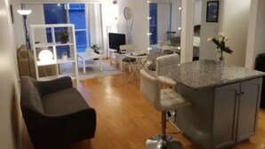 Ett modernt vardagsrum med en soffa, en matplats med bord och stolar, ett kök med en bardisk och en balkong med utsikt.