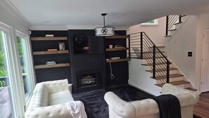 Uma sala de estar com um sofá branco, uma lareira, uma escada e uma estante de livros.