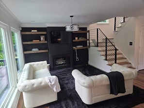 A living room with a white sofa, a fireplace, a staircase, and a bookshelf. - Your luxury East Atlanta oasis (Atlanta)