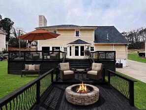 Eine Terrasse mit Gartenmöbeln, einem Feuerkorb und einem überdachten Bereich mit Sonnenschirm.