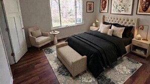 Quarto com cama grande, mesa de cabeceira, cadeira, janela e obra de arte na parede.