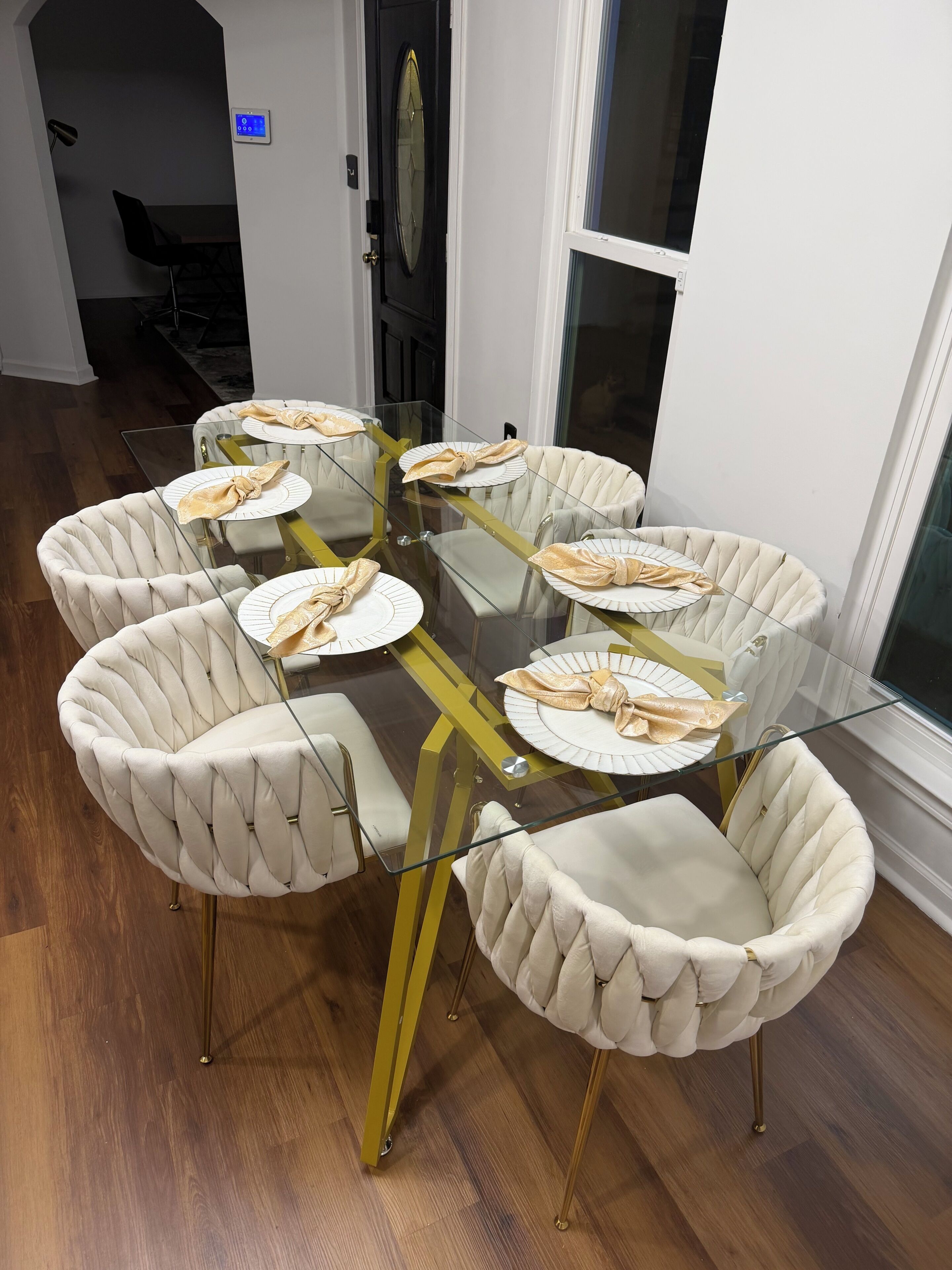 Un coin repas avec une table en verre entourée de fauteuils capitonnés, une porte dotée d’un clavier numérique et une vue par la fenêtre.
