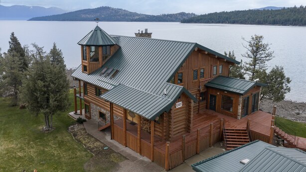 A large log cabin with a metal roof, a balcony, and a view of a lake.