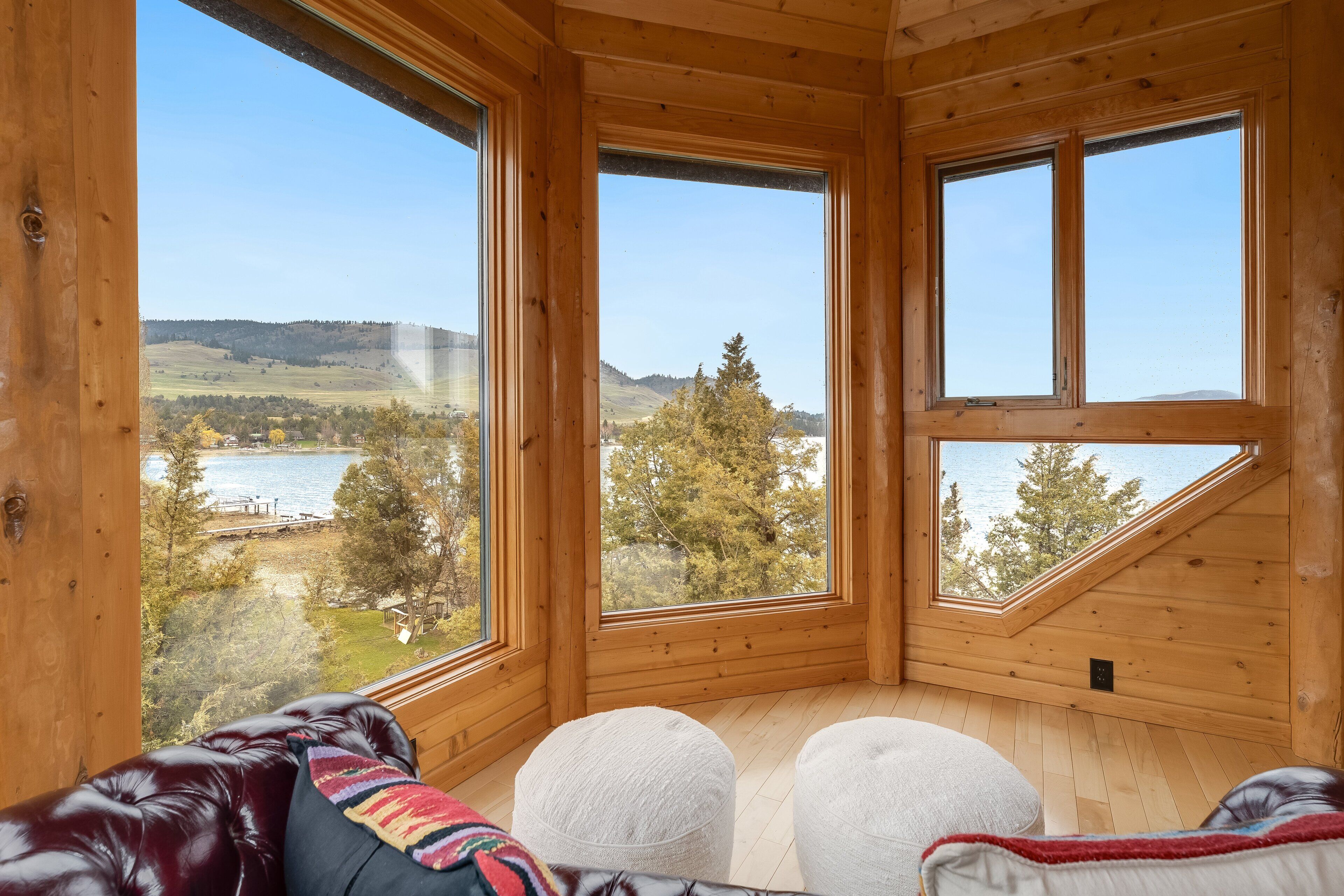 A wooden cabin with large windows, a leather couch, and ottomans.