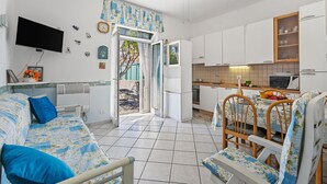 Un espace de vie compact comprenant un canapé, une table à manger, des chaises, un téléviseur, un coin cuisine et une porte donnant sur l’extérieur.