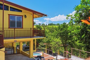 Ein gelbes Gebäude mit Balkon, Pool und üppiger Vegetation im Hintergrund.