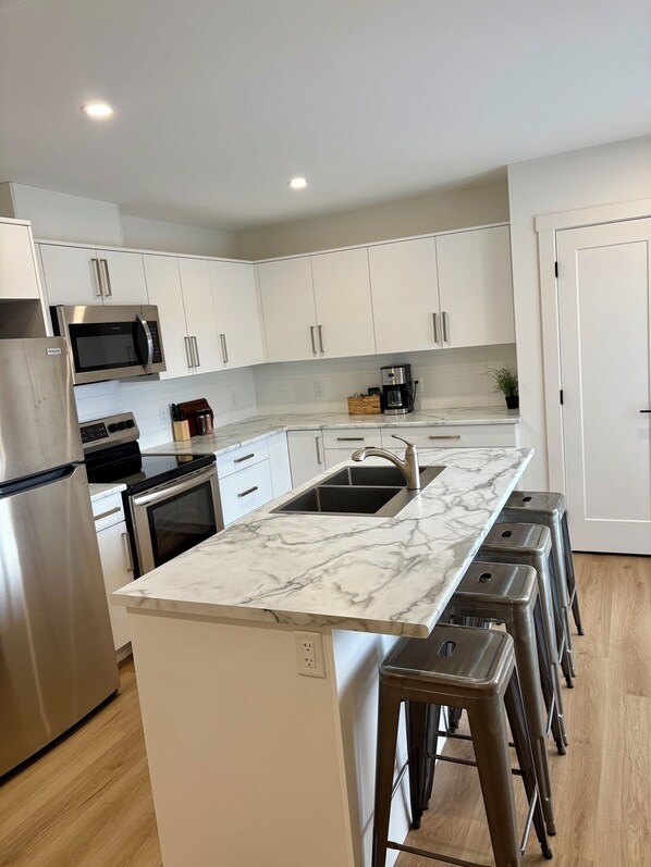 A modern kitchen with white cabinets, stainless steel appliances, a marble countertop, and a built-in sink.