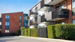 Un immeuble d’appartements moderne doté de balcons, d’une façade en briques et d’une haie bien entretenue.