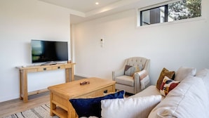 Un salon moderne avec un téléviseur à écran plat, une table basse en bois, un canapé beige et un fauteuil.