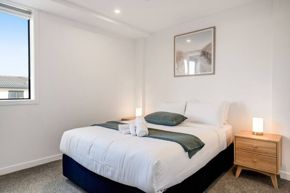 Une chambre à coucher bien rangée, avec un lit, des tables de chevet, une lampe fixée au mur et un tableau encadré.