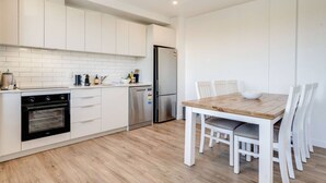 Une cuisine moderne avec des meubles blancs, un four encastré, un lave-vaisselle et un réfrigérateur.