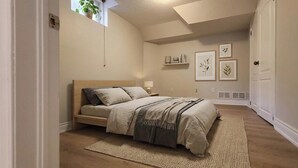 A bedroom with a bed, a window, a plant, and wall art.