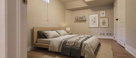 A bedroom with a bed, a window, a plant, and wall art.