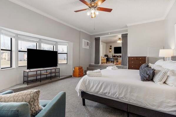 Een slaapkamer met een bed, een televisie, een plafondventilator en een raam.