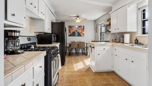 A kitchen with white cabinets, a stove, a refrigerator, and a dining area with chairs. - Owasso Home/ 5 beds 2 bath/ King (Owasso)