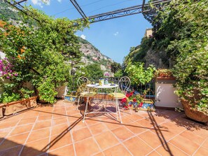 A patio with a table and chairs, surrounded by potted plants and a view of a hillside. - Positano Elegant Terrace (Positano)