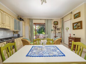 A dining area with a table set for four, surrounded by chairs, in a room with a kitchen and a view through a door. - Positano Elegant Terrace (Positano)