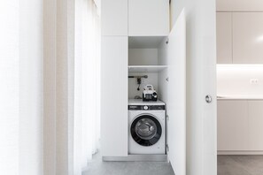 A compact laundry room with a front-loading washing machine, a drying rack, and a small shelf with a toy car. - GuestReady - Seaside retreat in Matosinhos (Matosinhos)