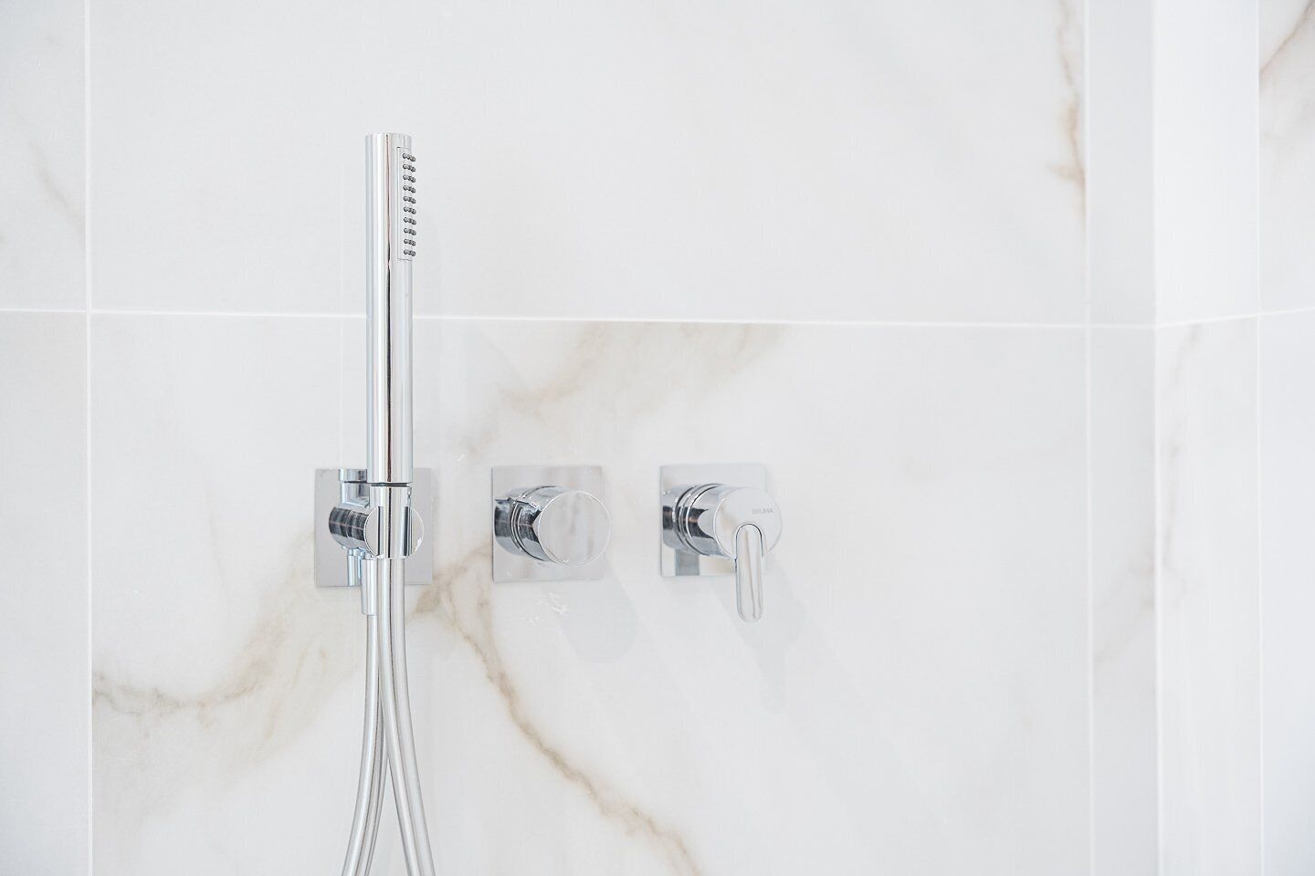 A bathroom with a shower, a faucet, and a control panel.