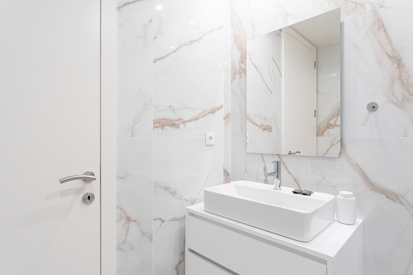 Un baño con pared de mármol, un lavamanos, un espejo y una puerta.